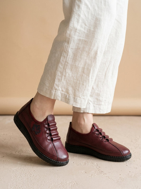 Detalle de los zapatos Valeria en burdeos puestos, con cordones elásticos y hoja bordada